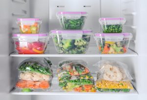 Posode in plastične vrečke, napolnjene s sadjem in zelenjavo v hladilnikus sadjem in zelenjavo v hladilnikuz zamrznjeno zelenjavo v hladilniku