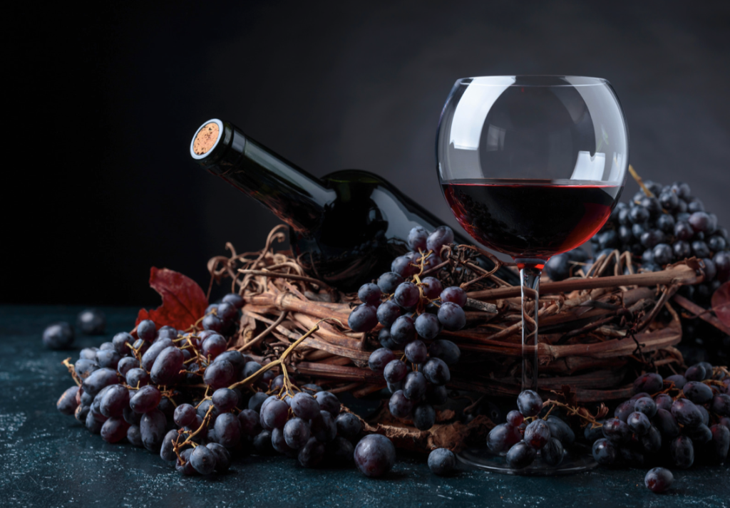 Rdeče vino v kozarcu, buteljka in rdeče grozdje