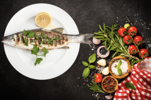 Pečena riba na krožniku in ob strani mediteranska zelišča