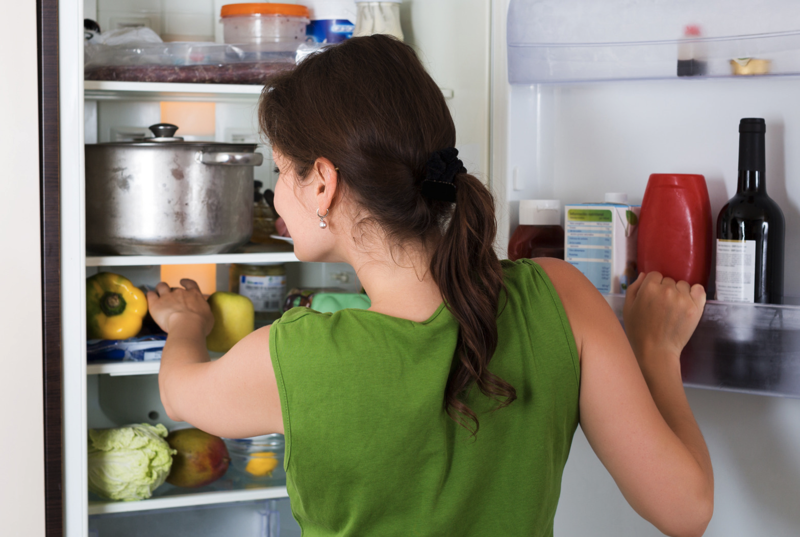 Ženska stoji pred odprtim hladilnikom in gleda vanj