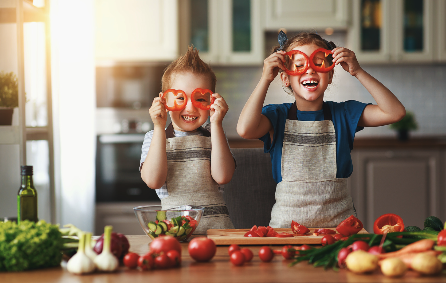 Dva otroka v kuhinji režeta zelenjavo in si pred oči postavita narezano papriko.