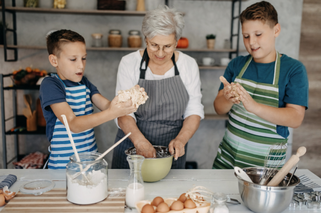 V kuhinji je babica z dvema vnukoma. skupaj pripravljajo kruh.